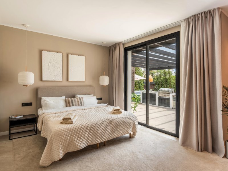 Charming bedroom in a cozy beach villa, just steps from the sea, featuring a peaceful design with soft, neutral colors, comfortable furnishings, and direct access to a private terrace with stunning ocean views, blending indoor comfort with outdoor serenity.
