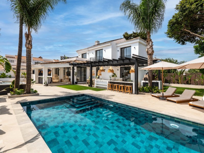 Charming facade of a cozy beach villa, just steps from the sea, showcasing a modern yet relaxed architectural design, with large windows, a welcoming entrance, and a seamless connection to the surrounding coastal landscape.