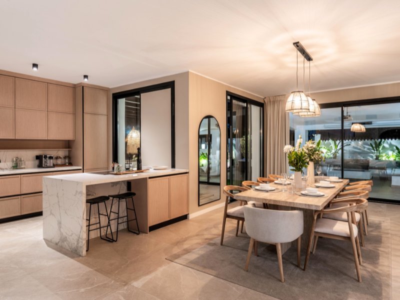 Bright and airy kitchen and dining room in a cozy beach villa, just steps from the sea, featuring modern appliances, open shelving, and a spacious dining area with large windows that provide stunning ocean views, creating a perfect setting for both cooking and entertaining.