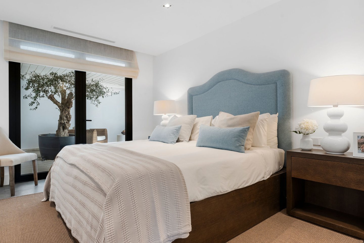 Elegant bedroom in a frontline golf villa in Nueva Andalucia, featuring a spacious layout with modern furniture, soft lighting, and large glass doors leading to a private terrace. The terrace offers breathtaking views of the lush golf course, creating a peaceful and luxurious retreat.