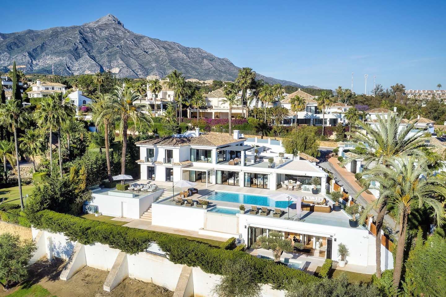 Stunning facade of a frontline golf villa in Nueva Andalucia, showcasing contemporary architecture with clean lines, large windows, and a spacious outdoor area. The villa is beautifully integrated into its lush green surroundings, offering a serene and luxurious atmosphere with views of the pristine golf course.
