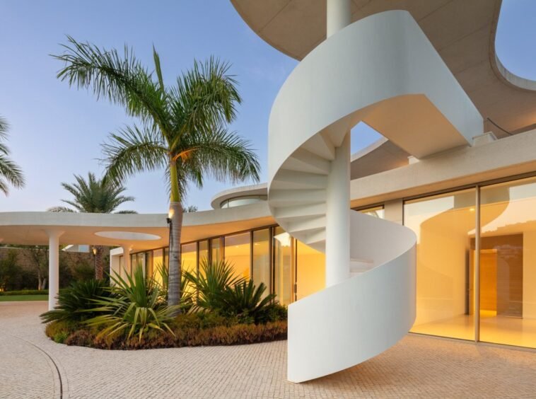 Striking facade of a futuristic villa in Finca Cortesín, Marbella, designed by Vicens Ramos, featuring innovative architecture with sleek lines, expansive glass panels, and bold geometric shapes, blending modern luxury with the villa’s natural surroundings to create a stunning visual impact.