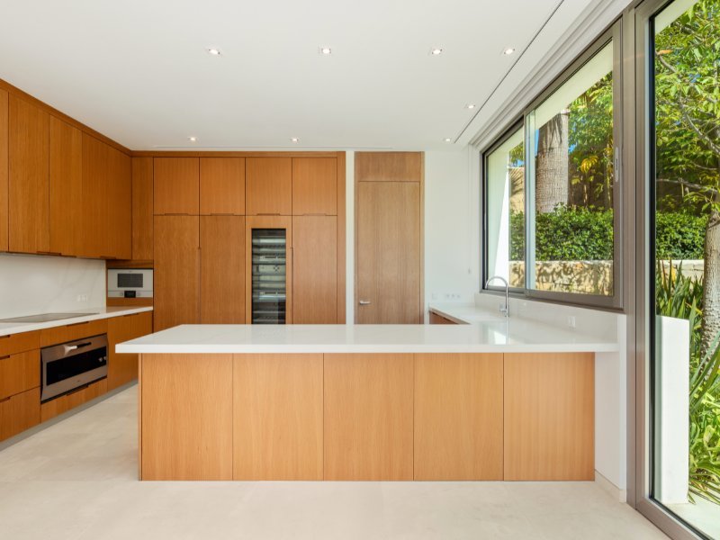 A modern, open-concept kitchen with sleek, high-end appliances, a large island with a built-in sink, and a stylish design featuring marble countertops and wood accents. The space is bright and spacious, with contemporary lighting and floor-to-ceiling windows offering views of the surrounding landscape.