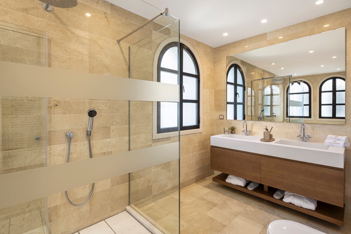 An opulent bathroom featuring classic Andalusian design elements, with intricate marble finishes, a freestanding bathtub, and a spacious walk-in shower. The room is elegantly illuminated by chandeliers and soft lighting, creating a luxurious and timeless ambiance.