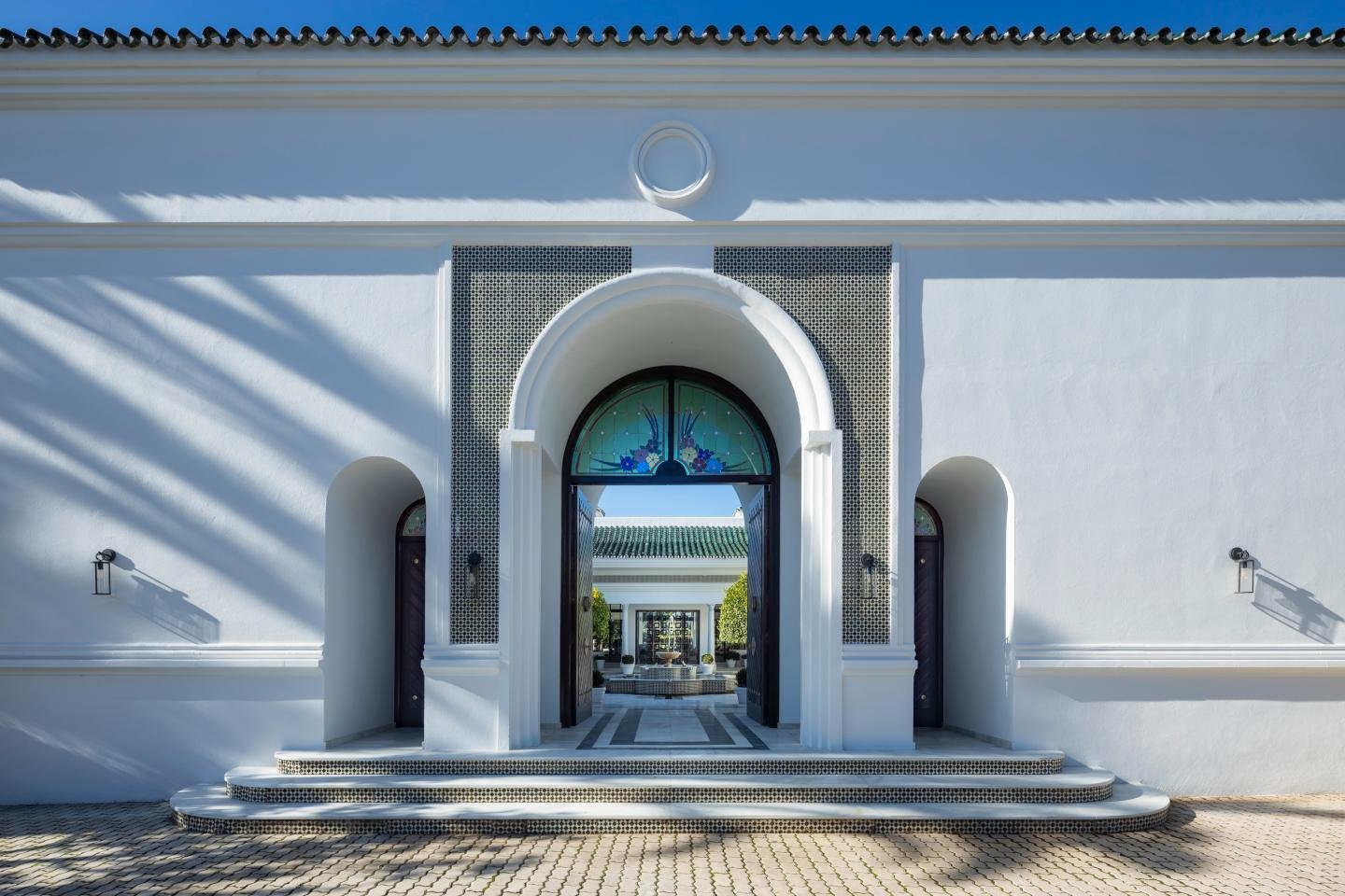 Grand entrance of a majestic Andalusian palace in Marbella, featuring ornate doors, a sweeping staircase, and intricate architectural details, setting the tone for the luxurious and timeless beauty that defines the property.