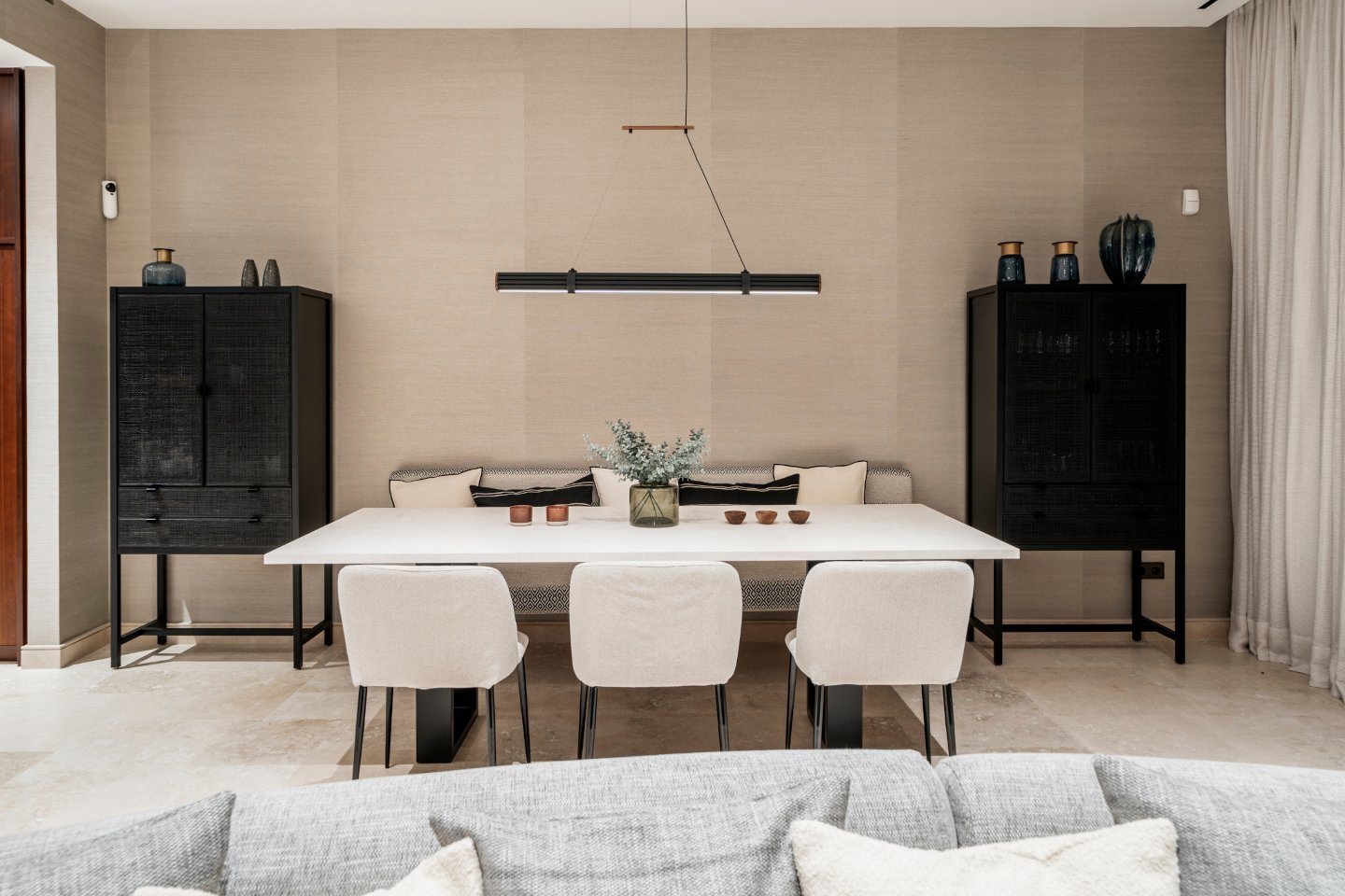 Elegant dining room in a modern villa in Nueva Andalucía, featuring a stylish dining table with sleek, contemporary chairs, and an open, airy atmosphere. Large windows allow natural light to flood the space, offering beautiful views of the surrounding landscape. The minimalist design and neutral tones create a sophisticated and inviting environment for dining and entertaining.