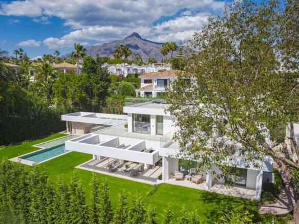 Stunning facade of a modern villa in Nueva Andalucía, featuring clean architectural lines, large windows, and a harmonious blend of sleek, contemporary design elements. The villa’s exterior is complemented by lush landscaping, creating an elegant and inviting first impression of luxurious living in a tranquil setting.