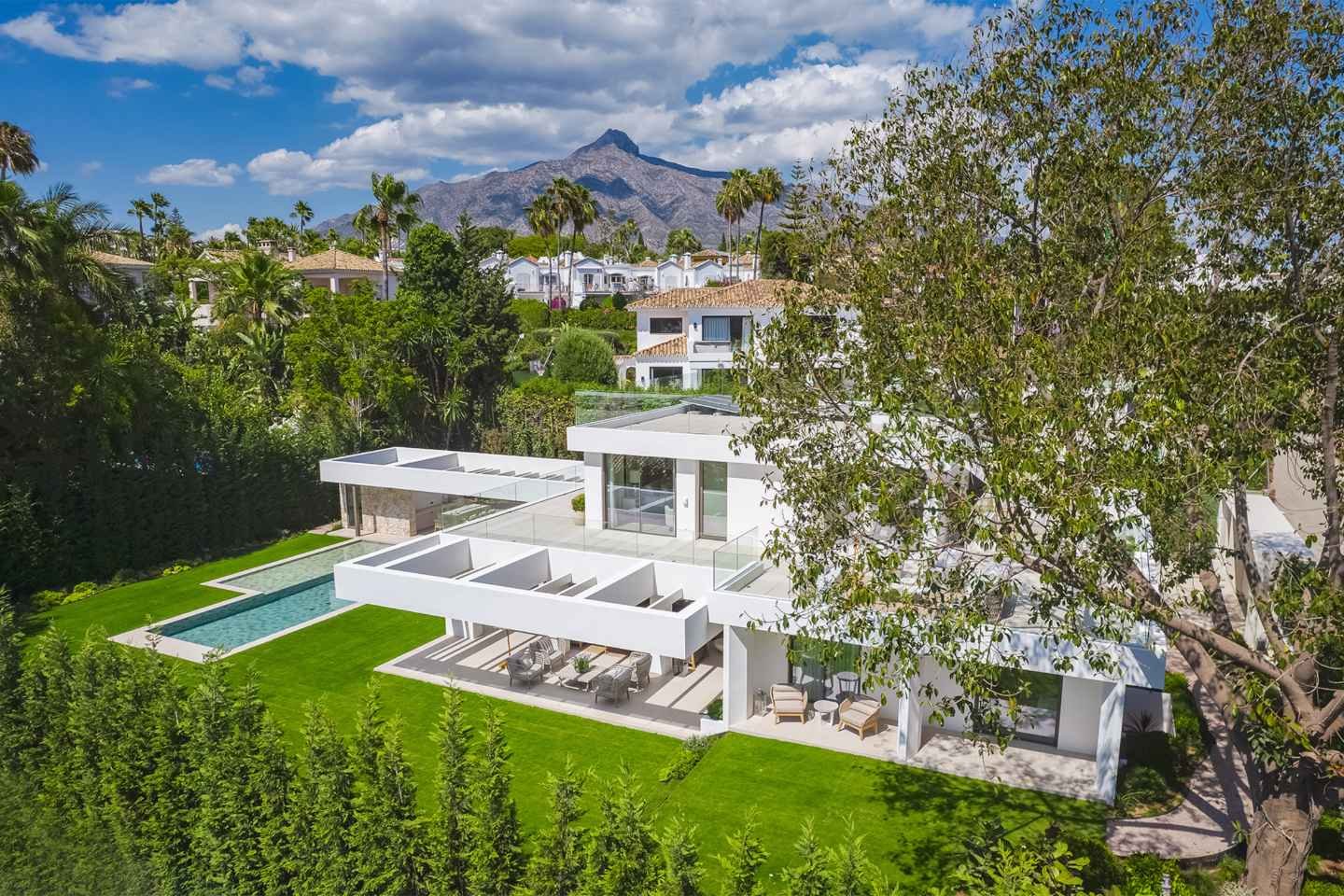 Stunning facade of a modern villa in Nueva Andalucía, featuring clean architectural lines, large windows, and a harmonious blend of sleek, contemporary design elements. The villa’s exterior is complemented by lush landscaping, creating an elegant and inviting first impression of luxurious living in a tranquil setting.