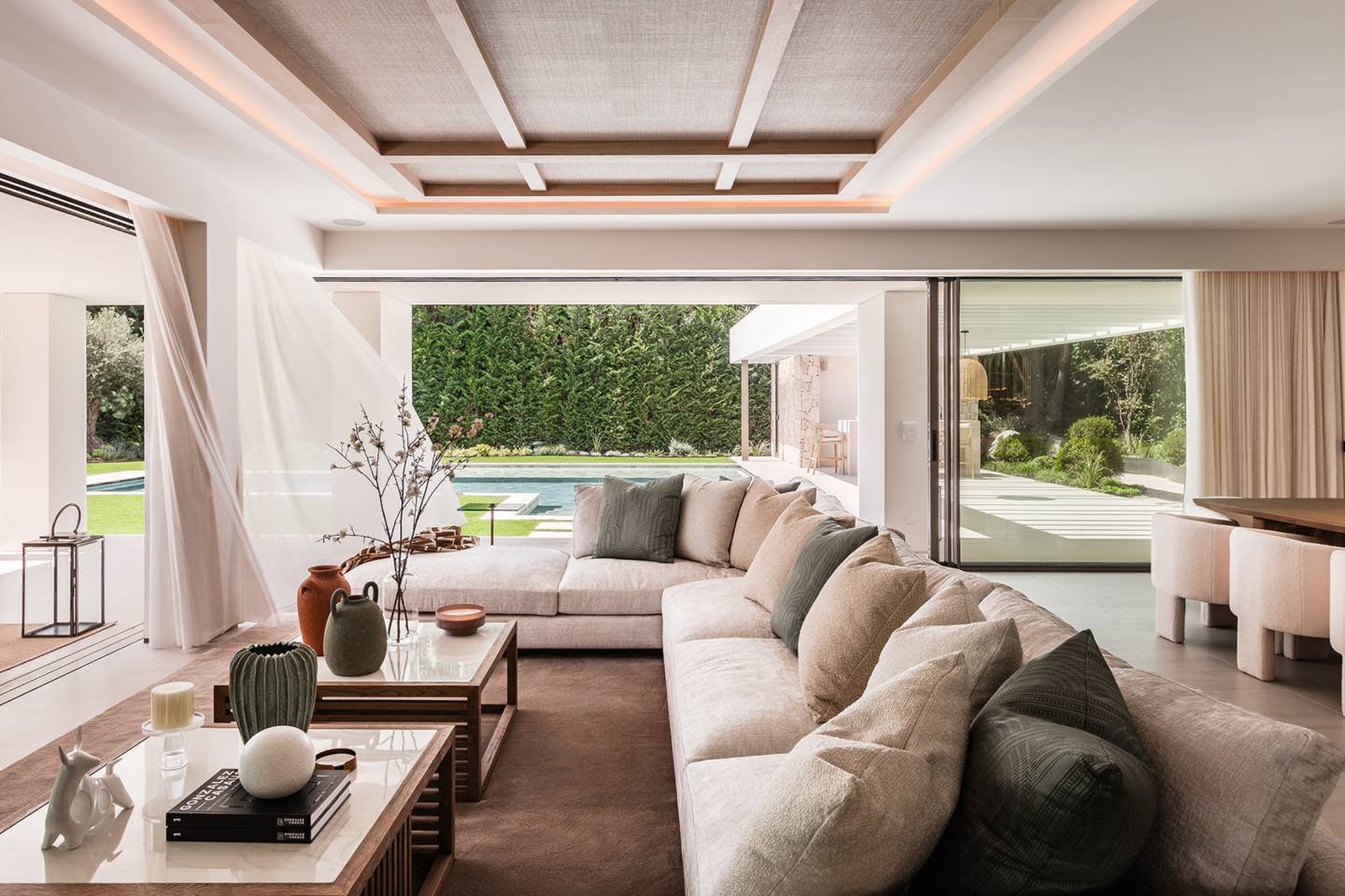 Spacious living and dining area in a modern villa in Nueva Andalucía, featuring a seamless open-plan design with elegant, contemporary furnishings. Large windows allow natural light to flood the space, highlighting the sleek finishes and neutral tones. The area blends comfort and luxury, creating a stylish and inviting atmosphere for both relaxation and entertaining.