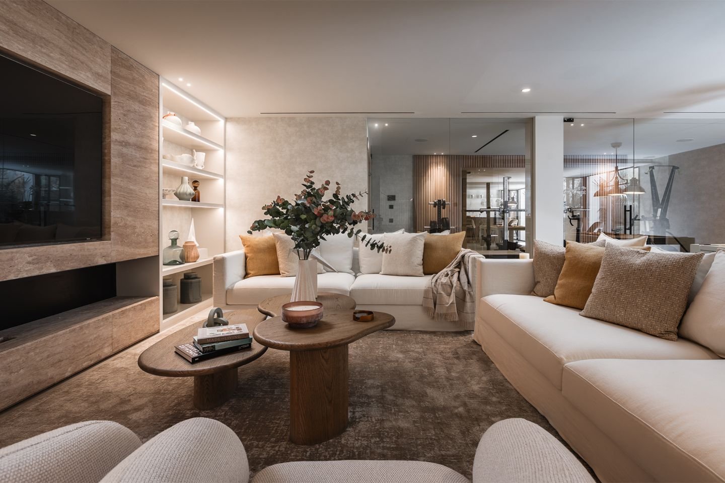 A sophisticated TV room with plush, contemporary seating, a large wall-mounted flat-screen TV, and ambient LED lighting. The space features sleek modern decor, neutral tones, and a cozy yet elegant atmosphere designed for entertainment and relaxation.